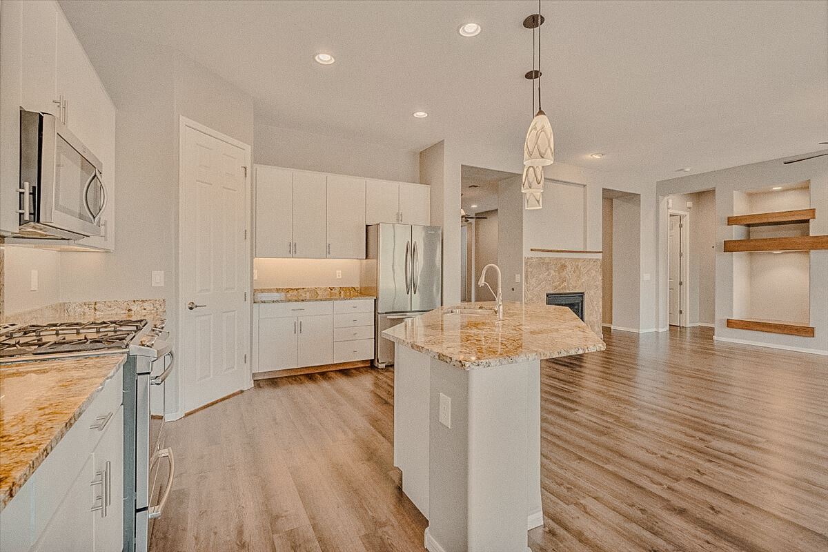 Open kitchen with a granite island and white cabinets looking toward a two-way fireplace in a vacant single-level home in Lone Mountain, Cave Creek, Arizona